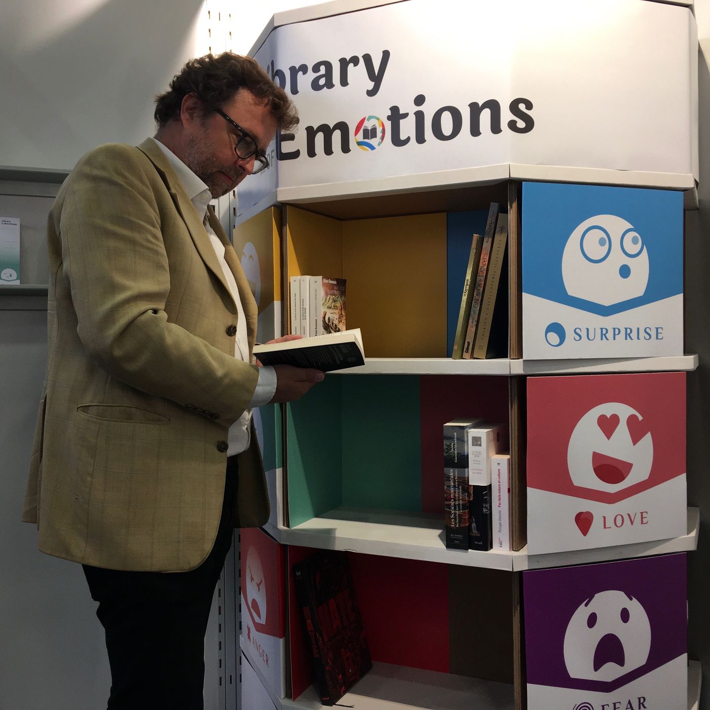 Un lecteur feuillette un livre devant une Library of Emotions, ses cases colorées par émotion